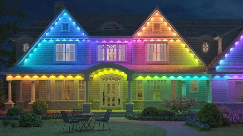 House lit with rainbow-colored holiday lights at night, with a front porch and yard furniture