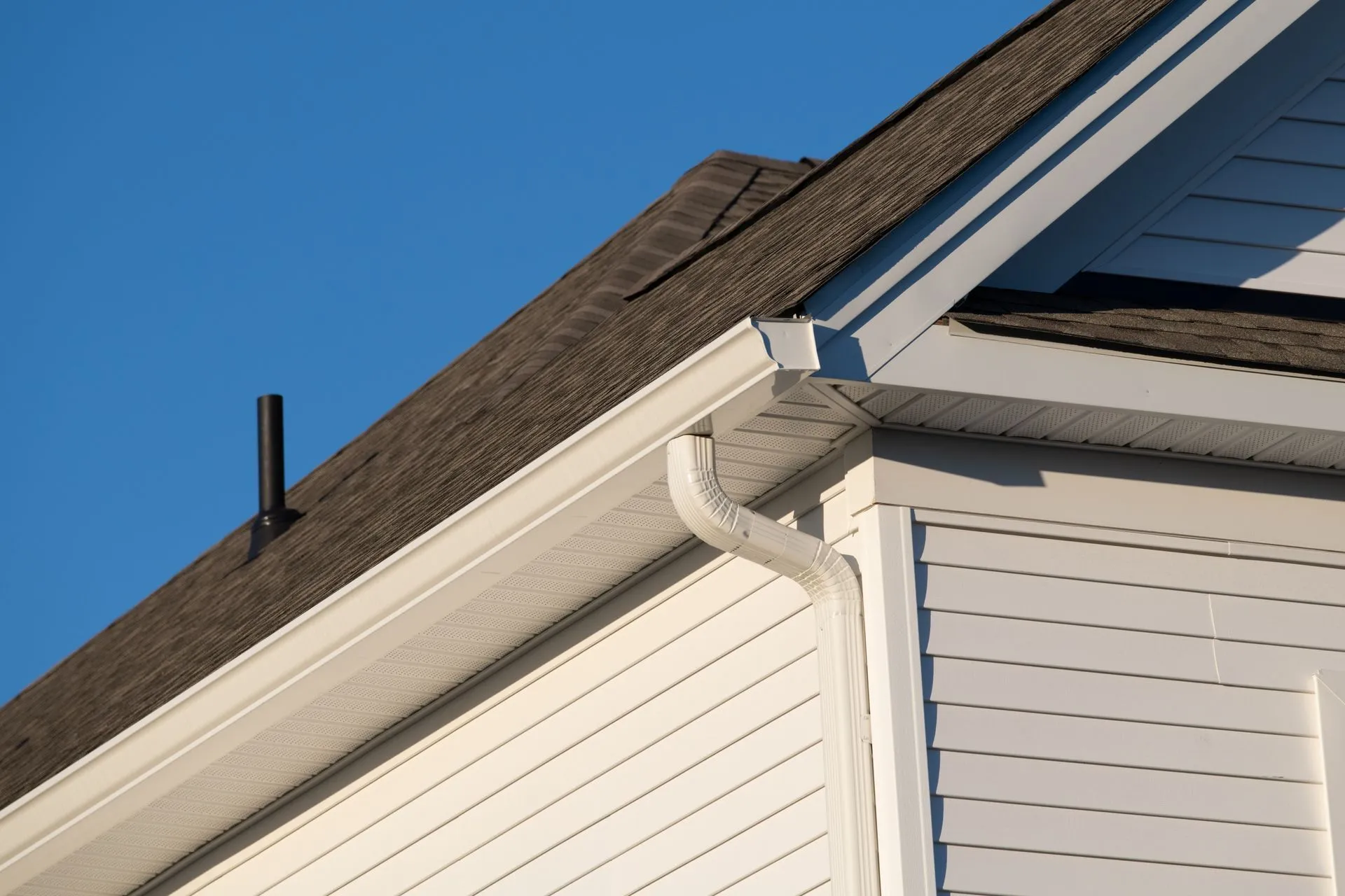 White house roof and gutters against a clear blue sky