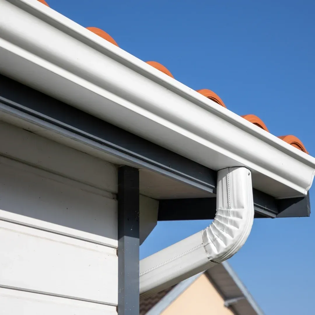 White gutter and downspout on house roof against blue sky