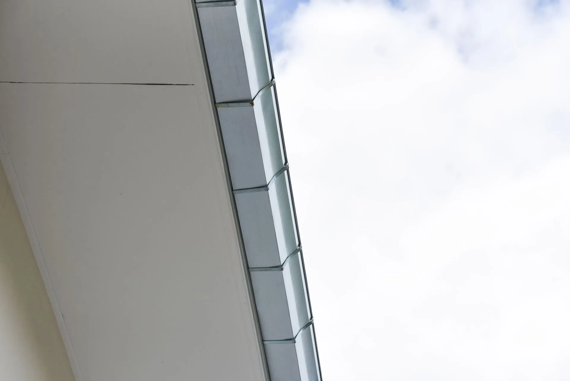 A close up of a gutter on the side of a building with a cloudy sky in the background.