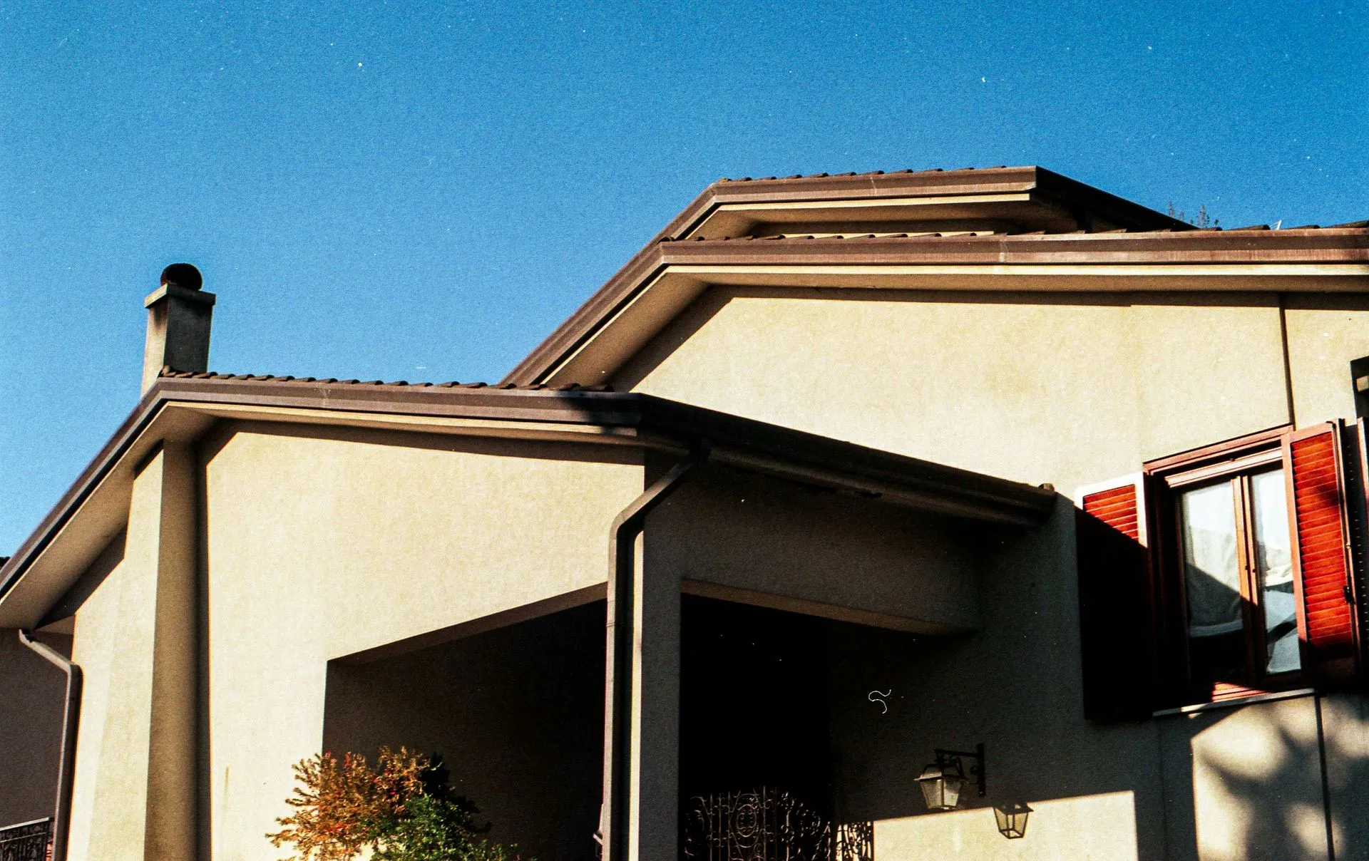 Suburban house exterior with beige walls, brown roof, and a covered porch under blue sky