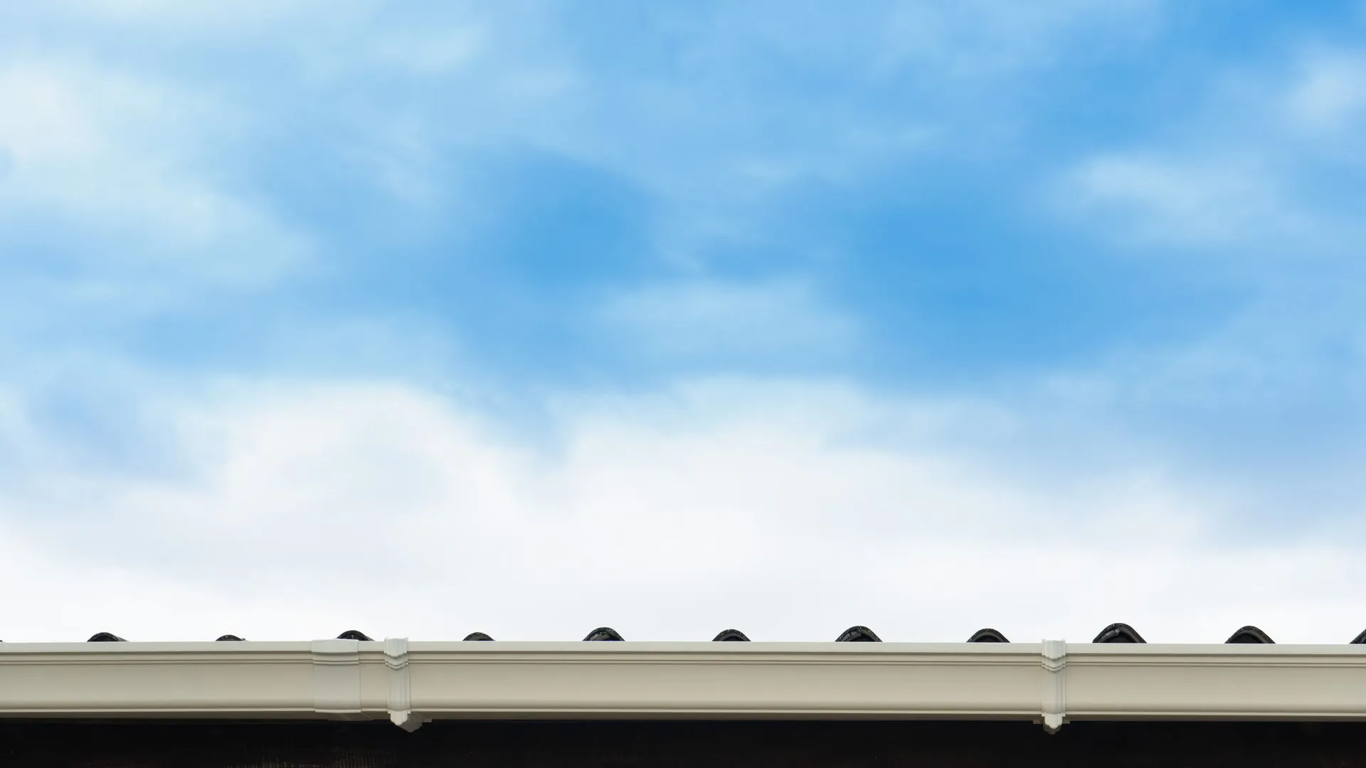 A close up of a gutter on a roof with a blue sky in the background.