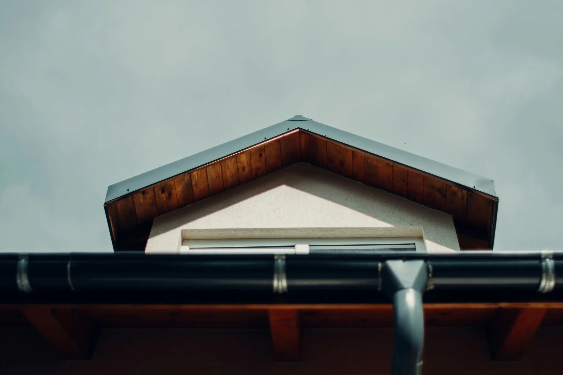 Close-up of a house roof with wooden eaves and a black gutter against a cloudy sky