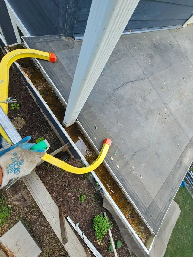Gloved hand holding yellow railing on a porch beside white post and concrete steps