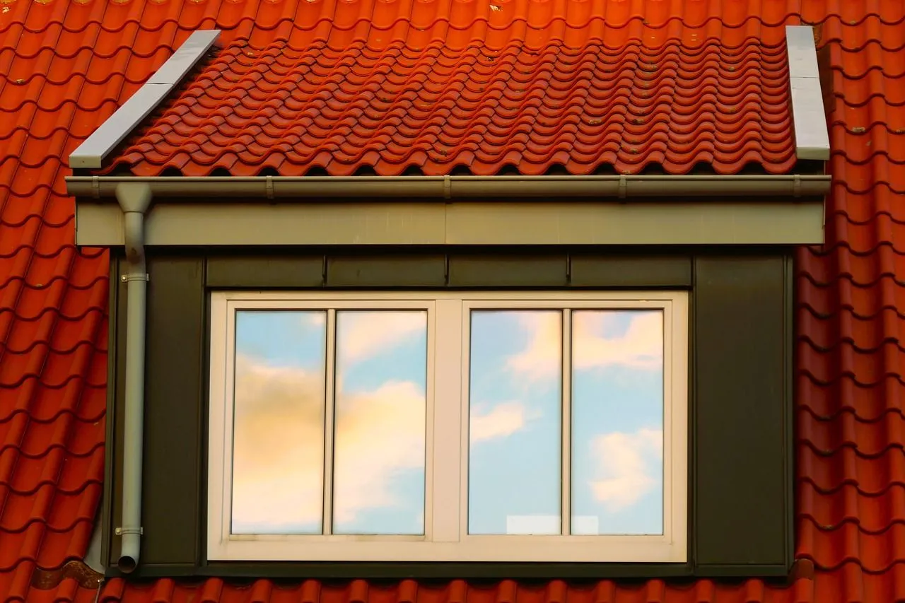 Small dormer window with white frames on a red tiled roof under a cloudy sky.