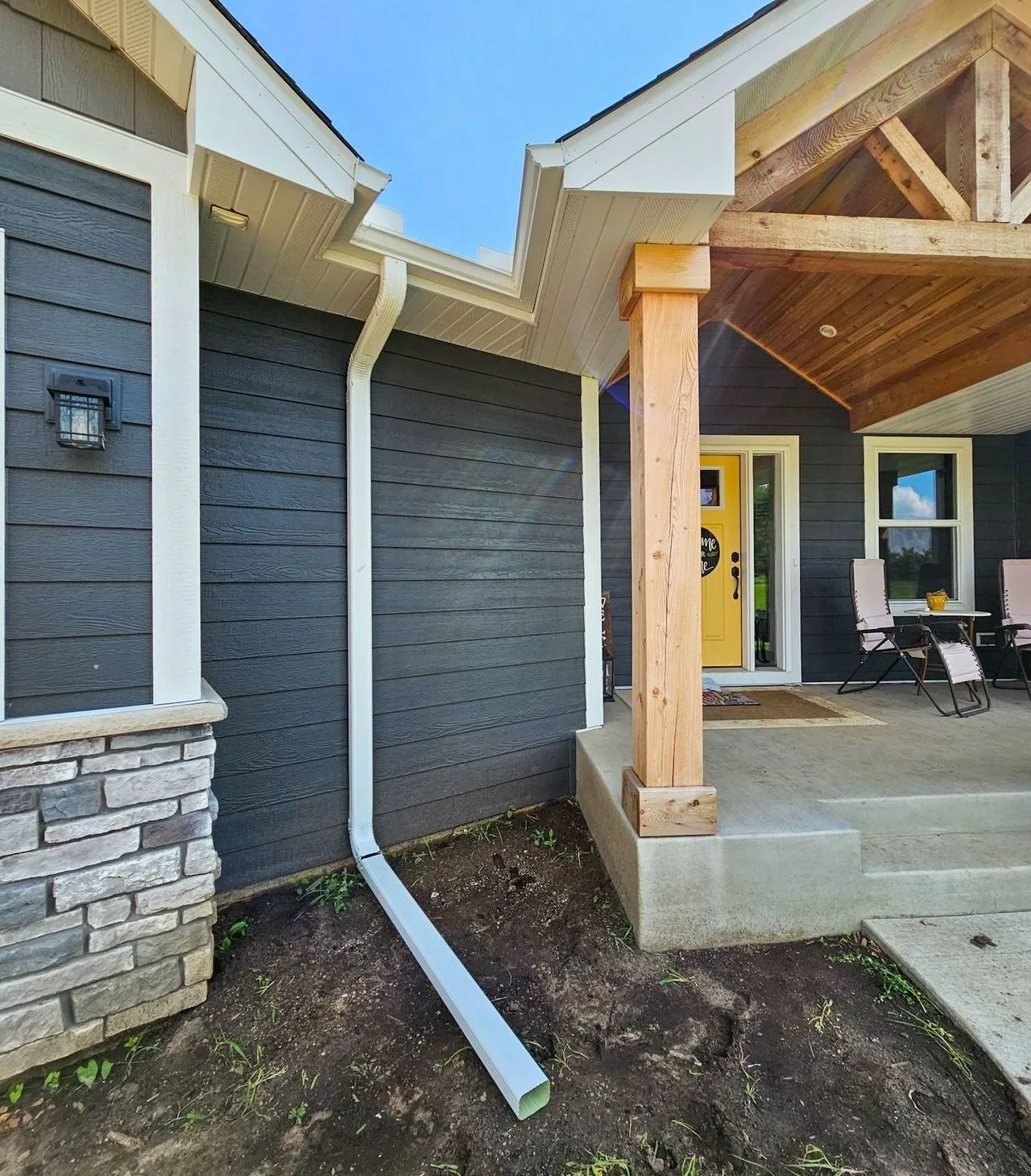 Downspout extension beside gray house exterior near front porch and concrete entry