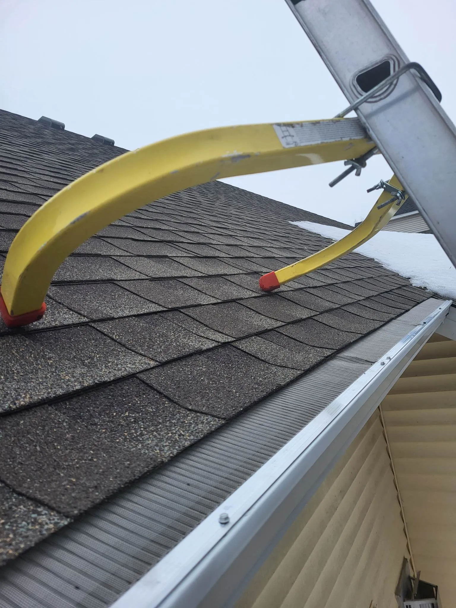 Damaged yellow awning bent over a shingled house roof in snow