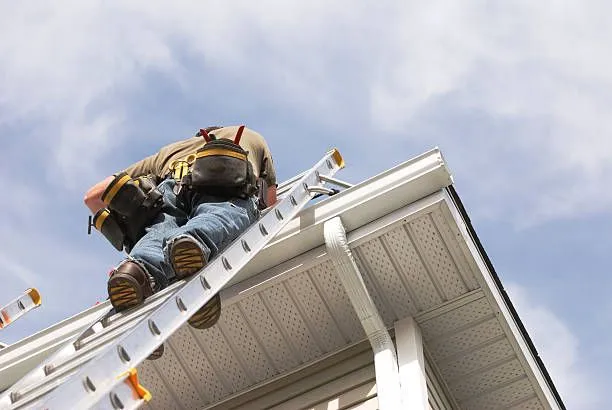 A man is cleaning a gutter on the roof of a house.