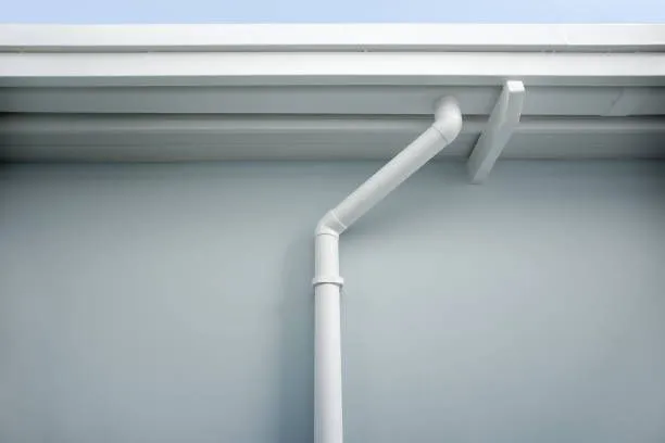 A white gutter on the side of a building with a blue sky in the background.